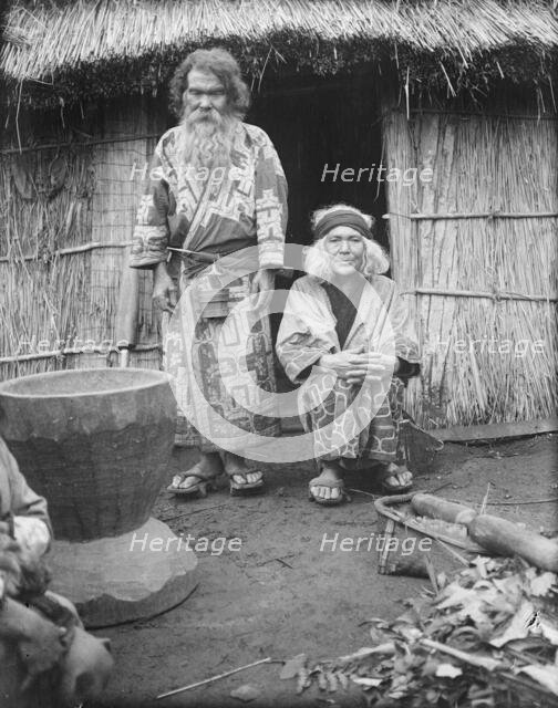 Ainu man and seated woman at the entrance of a hut, 1908. Creator: Arnold Genthe.