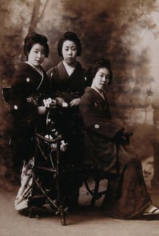 Three young women posing in a photographic studio, one seated on a bench..., early 20th century. Creator: Unknown.