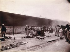 A group of men stand around the body of a man laid out on a pyre of logs during a Hindu...,  1896/97 Creator: Unknown.