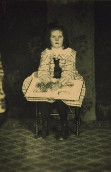 Girl in a plaid dress seated with a book in her lap, c1900. Creator: Mathilde Weil.