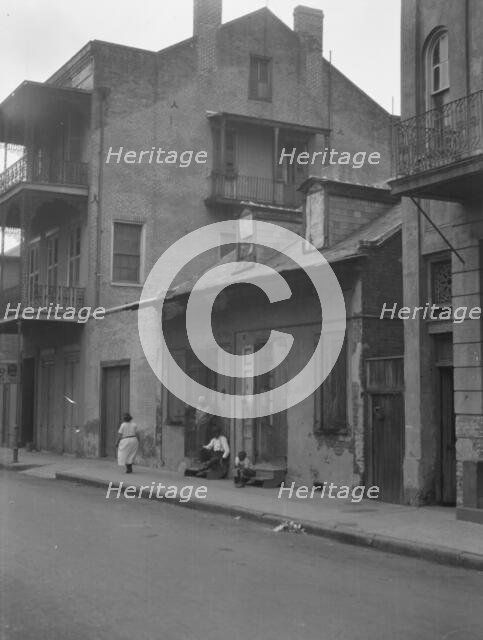 View from across street of a man and child sitting on steps and a woman walking down..., c1920-1926. Creator: Arnold Genthe.