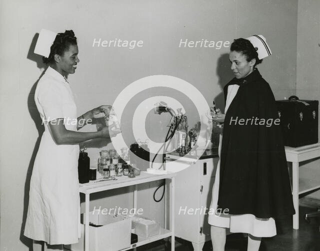 Captain Mary L. Petty, Chief Nurse, holding a glass bottle and showing it to 2nd Lieut..., 1939 - 19 Creator: Unknown.