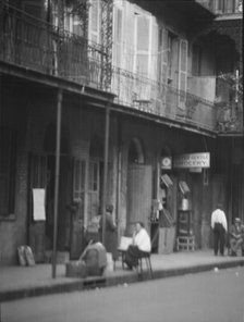 View from across street of people under a covered sidewalk, New Orleans, between 1920 and 1926. Creator: Arnold Genthe.