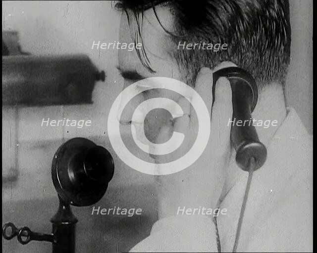 A British Man Holding a Candlestick Telephone Receiver to His Ear and Speaking Into the..., 1939. Creator: British Pathe Ltd.