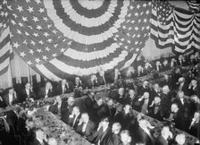 Banquet Scene with Flag Draping And Men Seated Holding Up Listening Device To One Ear, c1913-1917. Creator: Harris & Ewing.