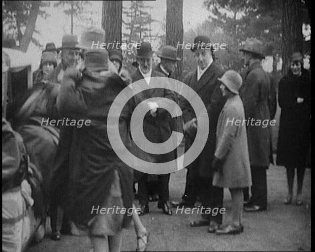 Female Civilian Helping Another Female Civilian to Put on a Coat in Front of a Car and a..., 1920. Creator: British Pathe Ltd.