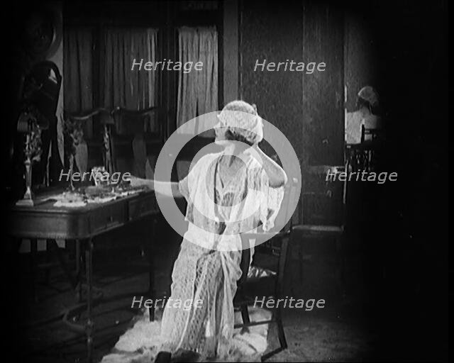 Female Civilian Seating in Front of a Dressing Table Wearing a Nightgown and Boudoir Cap, 1920. Creator: British Pathe Ltd.