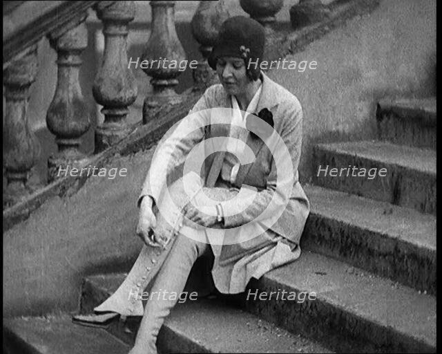 Female Civilian Doing up the Buttons of Her Leather Boots Sitting on Steps Outdoors, 1920. Creator: British Pathe Ltd.