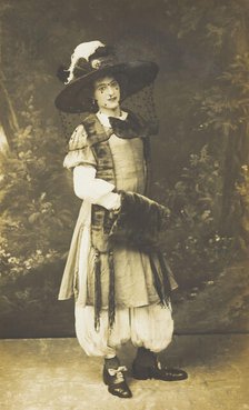 A man in drag wearing a very large hat with a veil, stands in front of a painted..., 1911. Creator: Unknown.