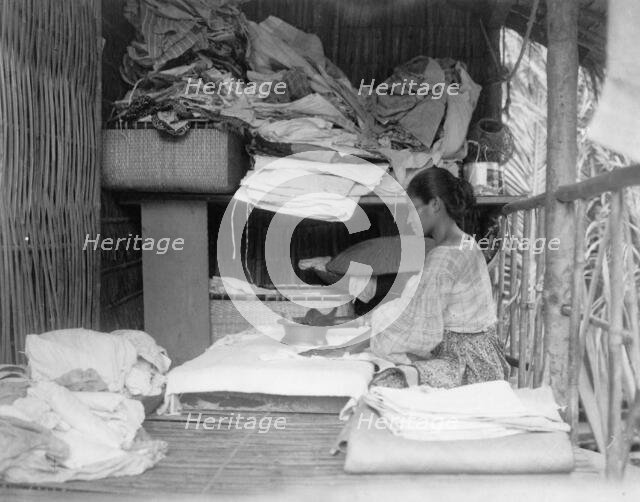 Javanese(?) woman sitting in room working with textiles at exhibit featuring foreign..., 1892. Creator: Frances Benjamin Johnston.