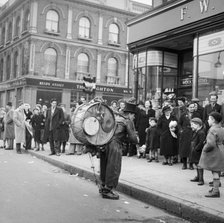One-man band performing in front of a crowd outside Woolworths, Camden, London, 1952. Artist: Henry Grant