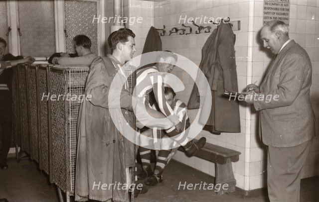 Footballers adjust their boots in the locker room, 1953. Artist: Unknown