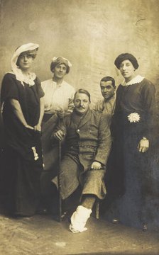 Four soldiers posing, three in drag, with an injured soldier seated in the centre, [1910-1919?]. Creator: Unknown.