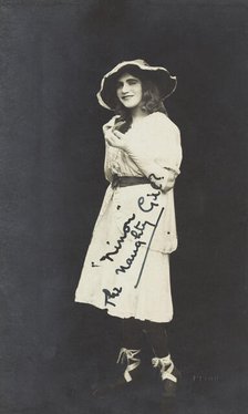 An amateur actor in drag, posing as 'Ninon', wearing a white dress and hat, [between 1920 and 1929?] Creator: Unknown.