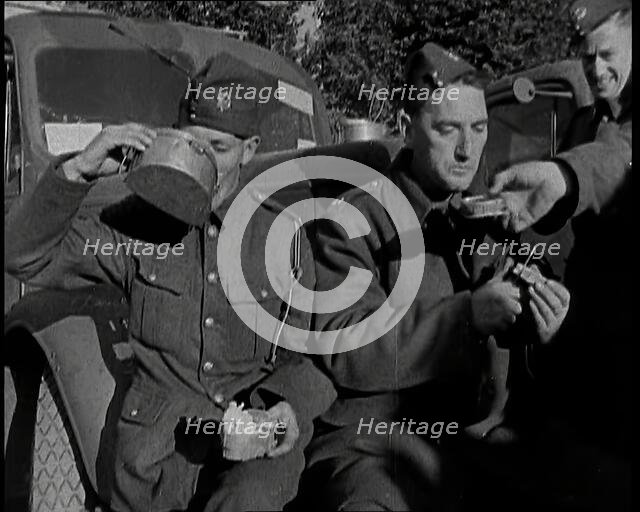 Two Male British Soldiers Sitting at  the Front of Army Trucks and Eating While Two Others..., 1939. Creator: British Pathe Ltd.