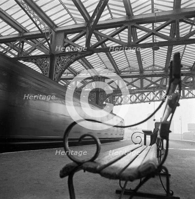 Looking along a bench with curved wrought iron arms on a platform at Waterloo Station, 1960-1972. Creator: John Gay.
