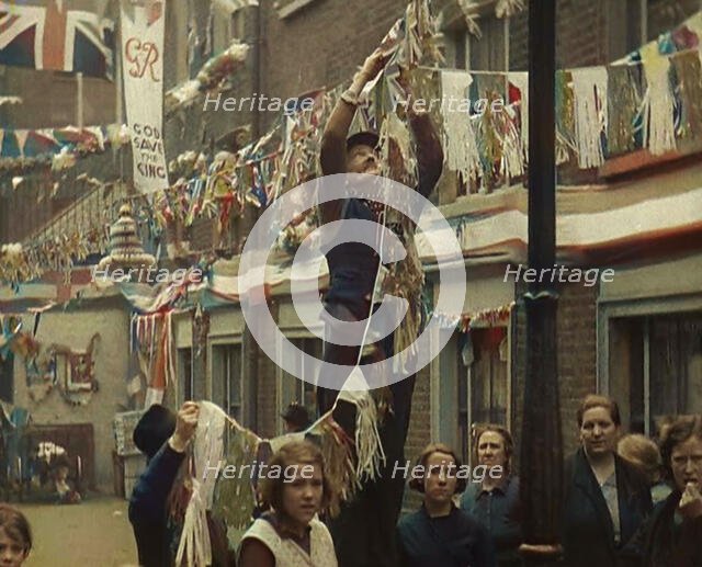 Man Hanging Bunting from a Lamp Post in a Street With Decorations For the Coronation of..., 1937. Creator: British Pathe Ltd.
