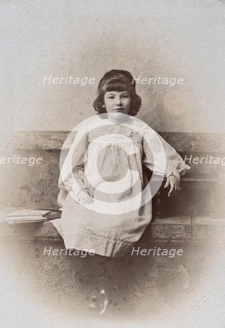A girl, sitting on a stone bench with a fan folded at her side, c1890s. Creator: Arthur Reston.