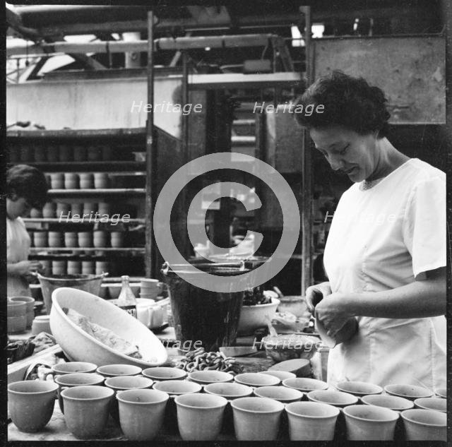 Woman fixing handles to mugs prior to firing in a pottery works, Stoke-on-Trent, 1965-1968. Creator: Eileen Deste.