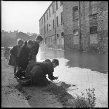 Children using a goldfish bowl to fish in the Caldon Canal, Hanley, Stoke-on-Trent, 1965-1968. Creator: Eileen Deste.