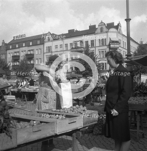 Woman buying potatoes from a fruit and vegetable stall in the market, Malmö, Sweden, 1947. Artist: Otto Ohm