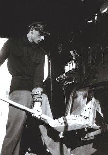 Stoker putting coal to a steam train engine.