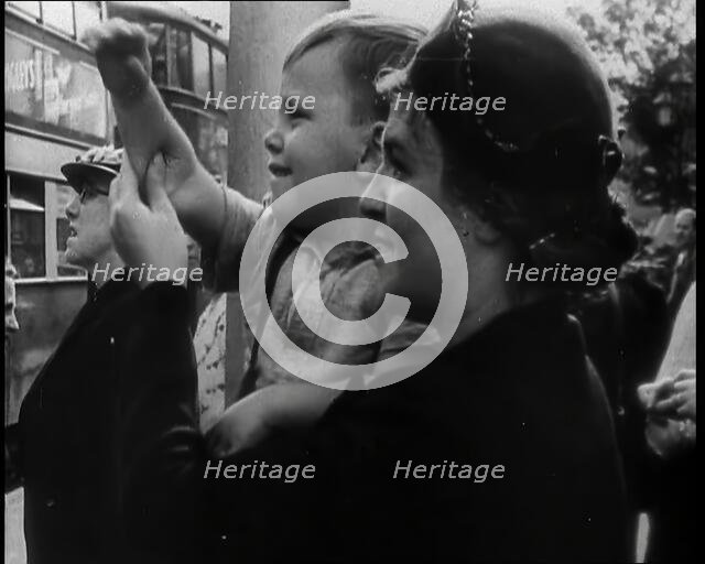 A British Woman Holding up a Young Boy Who is Waving in the Direction of a Bus as Other..., 1939. Creator: British Pathe Ltd.