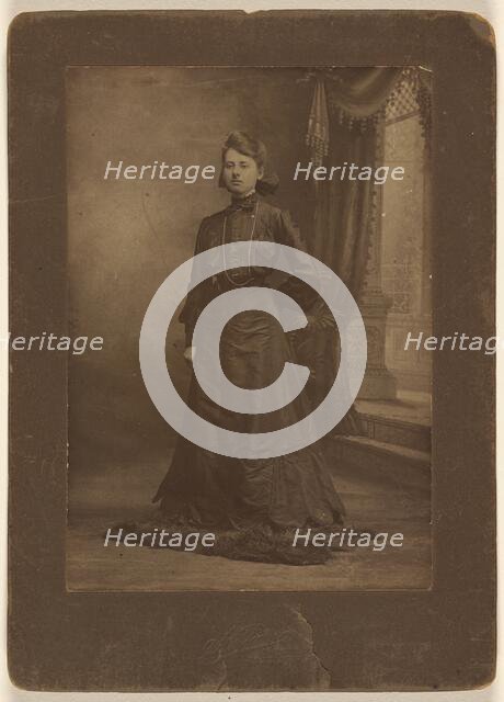 Portrait of a young woman in long black dress, standing, about 1900. Creator: George W Killian.