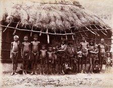 A group of adults and children standing in a line outside a bamboo hut with a thatched..., 1896/1897 Creator: Unknown.