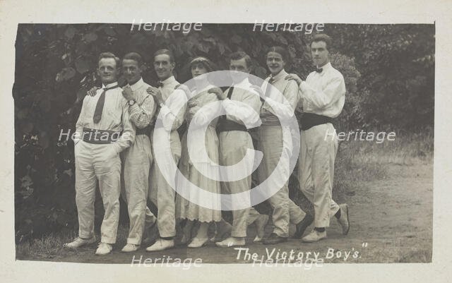 Entertainers, one in drag, pose in a line in front of foliage, [between 1910 and 1919?]. Creator: Unknown.