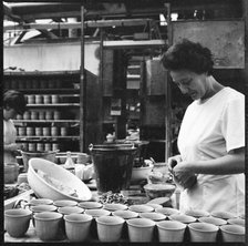 Woman fixing handles to mugs prior to firing in a pottery works, Stoke-on-Trent, 1965-1968. Creator: Eileen Deste.