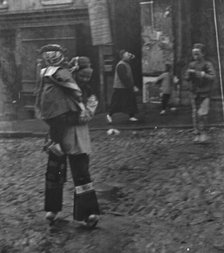 Woman carrying a child crossing a street, Chinatown, San Francisco, between 1896 and 1906. Creator: Arnold Genthe.