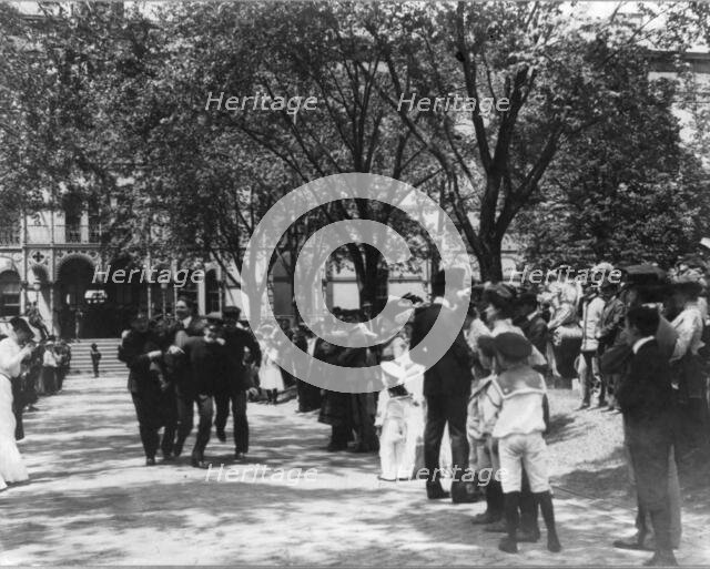 U.S. Naval Academy, Annapolis: 4 midshipmen carrying a man; crowd of guests along sidewalk, (1902?). Creator: Frances Benjamin Johnston.