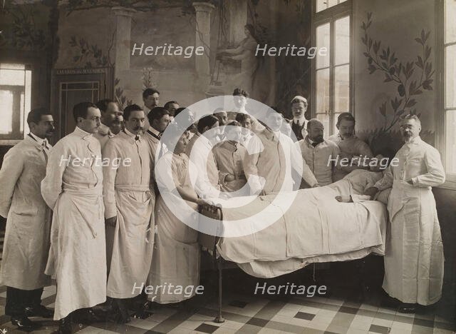 Medical staff standing round a woman patient in bed in a hospital ward, c1910. Creator: Freres Seeberger.