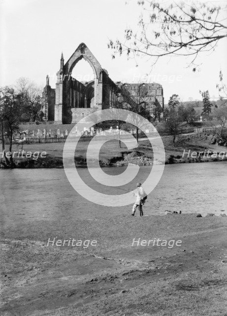 A fisherman on the River Wharfe in front of the ruins of Bolton Priory, North Yorkshire, 1940. Artist: Walter Scott.