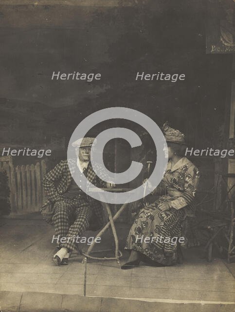 Two sailors, one in drag, sit on stage at a table, in front of very detailed scenery (1910-1919?). Creator: Unknown.