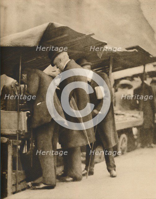 'At One of the Bookstalls of the Farringdon Road Market', c1935. Creator: Walter Benington.