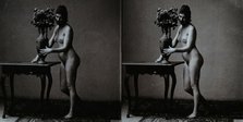 A young woman posing naked in a photographic studio, standing in front of a table on which..., c1900 Creator: Unknown.