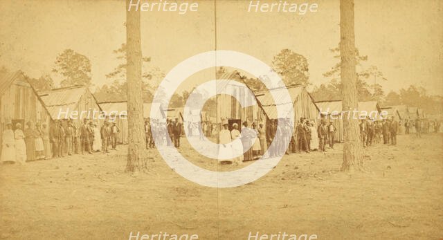 Group lined up in front of a row of shacks, (1868-1900?). Creator: Unknown.