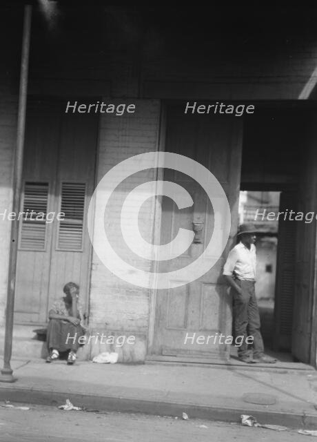 Woman sitting on steps and man standing in a doorway, New Orleans, between 1920 and 1926. Creator: Arnold Genthe.
