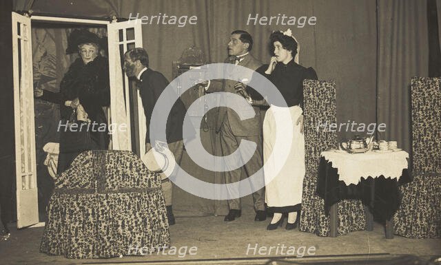 Amateur actors, one in drag, perform a scene on stage, [between 1910 and 1919?]. Creator: Unknown.