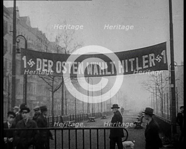 Men Walking Below Banner Reading: '1 Der Osten Wahlt Hitler 1' , 1933. Creator: British Pathe Ltd.