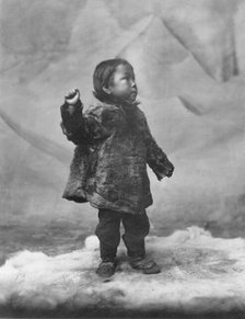 Eskimo child posing while standing on fur rug, between c1900 and c1930. Creator: Unknown.
