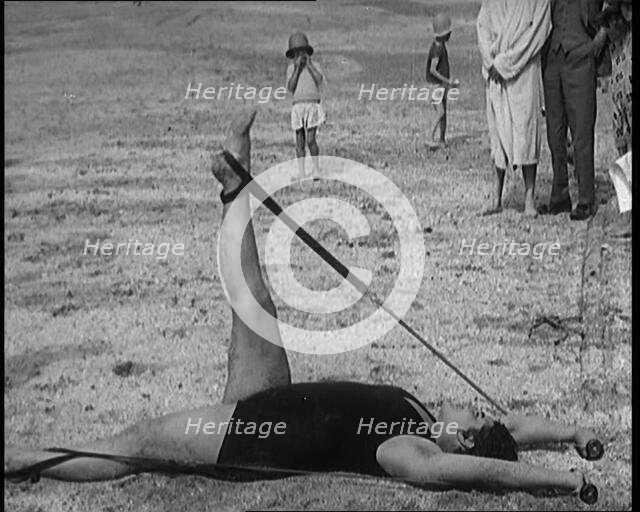 Female Civilian Laying on the Sand Exercising with an Elastic Band on a Beach, 1920. Creator: British Pathe Ltd.