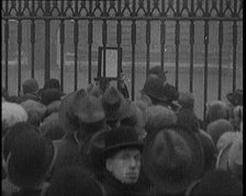 A Male Civilian Holding up a Bulletin from the Doctor to Crowds Gathering Outside..., 1929. Creator: British Pathe Ltd.