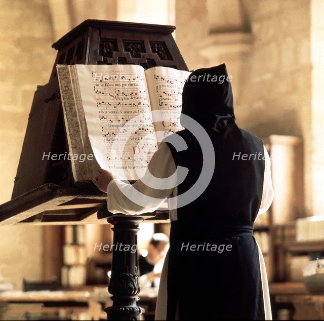 Benedictine monk consulting a song book from the Monastery of Poblet library.