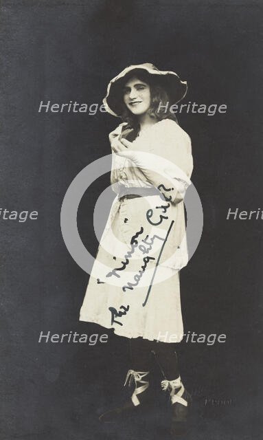 An amateur actor in drag, posing as 'Ninon', wearing a white dress and hat, [between 1920 and 1929?] Creator: Unknown.