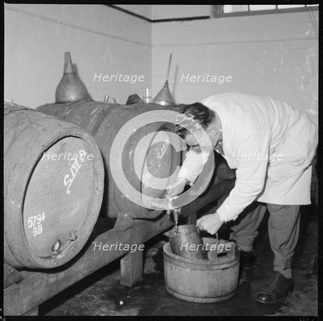Man drawing a sample of beer from a barrel, Burton upon Trent, Staffordshire, 1965-1968. Creator: Eileen Deste.