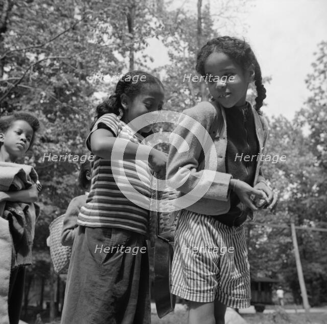 Girls adjusting each others' packs for a hike at Camp Fern Rock, Bear Mountain, New York, 1943. Creator: Gordon Parks.