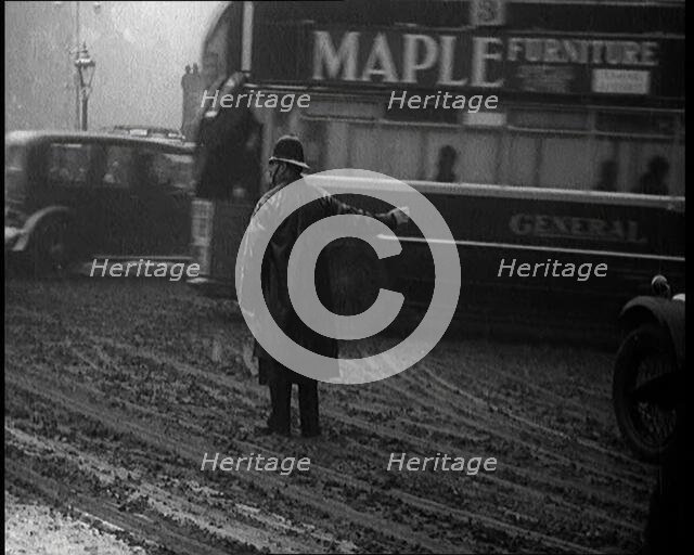 A Male Police Officer Directing the Traffic in the Snow, With His Back to the Camera, 1920s. Creator: British Pathe Ltd.